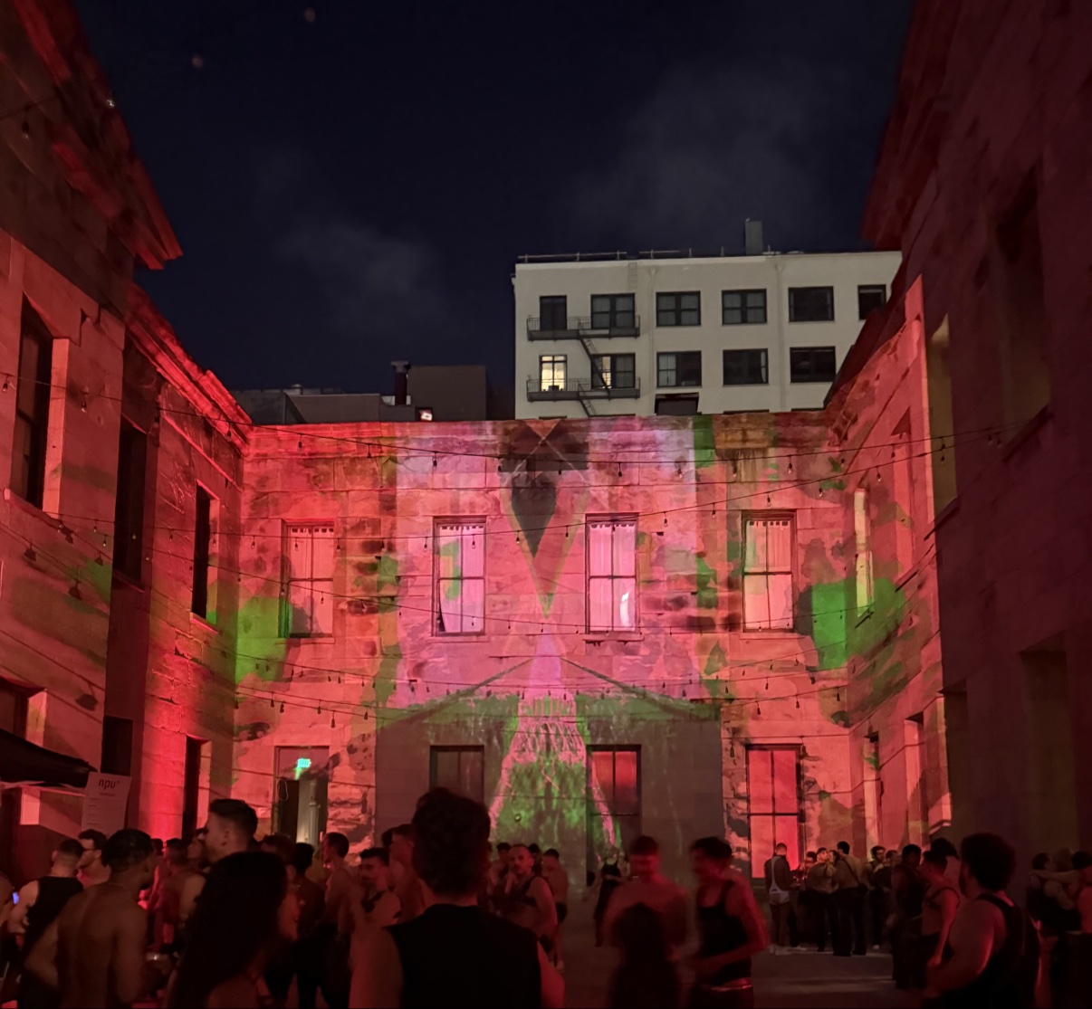 Crowd in the SF Mint courtyard at night, visuals projected across the building wall in red and green