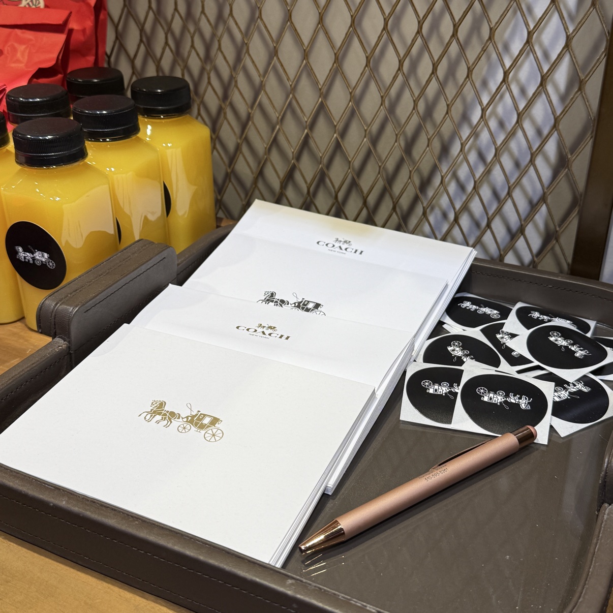 A tray with Coach stationery, stickers and a pen, beside bottles of orange juice