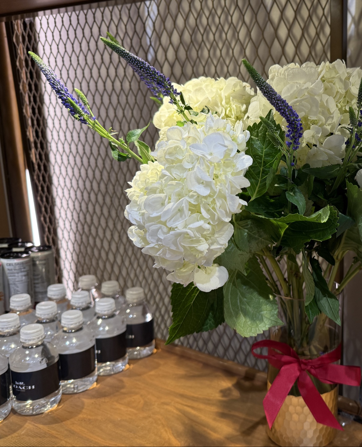 A white hydrangea arrangement beside Coach water bottles — the in-store refreshments setup