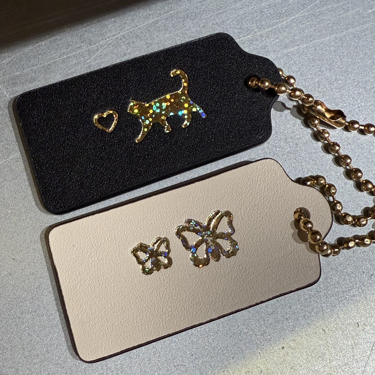 Two customized hangtags — a black one with a gold glitter cat and heart, and a cream one with butterflies