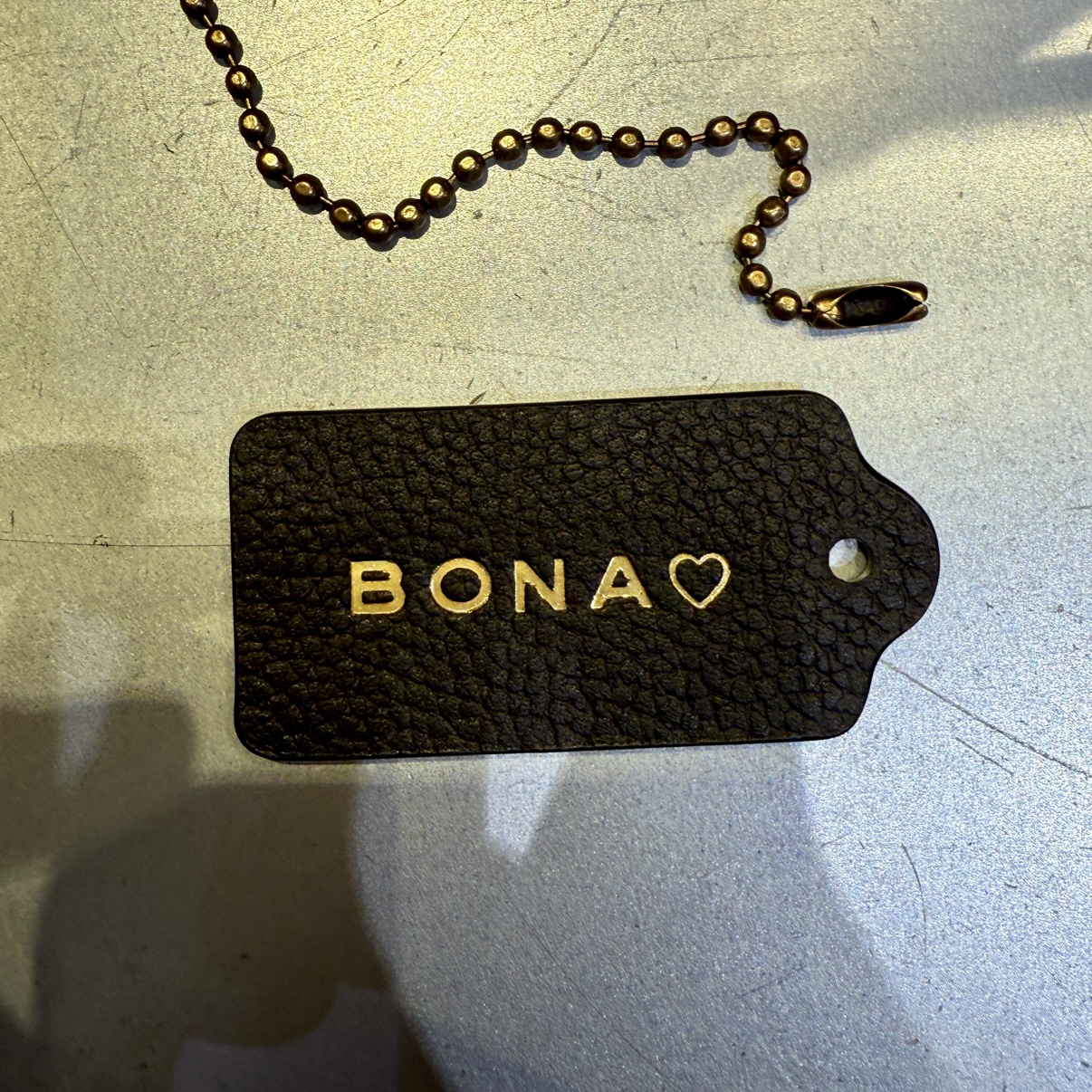 Black leather hangtag hot-stamped BONA with a heart, in gold