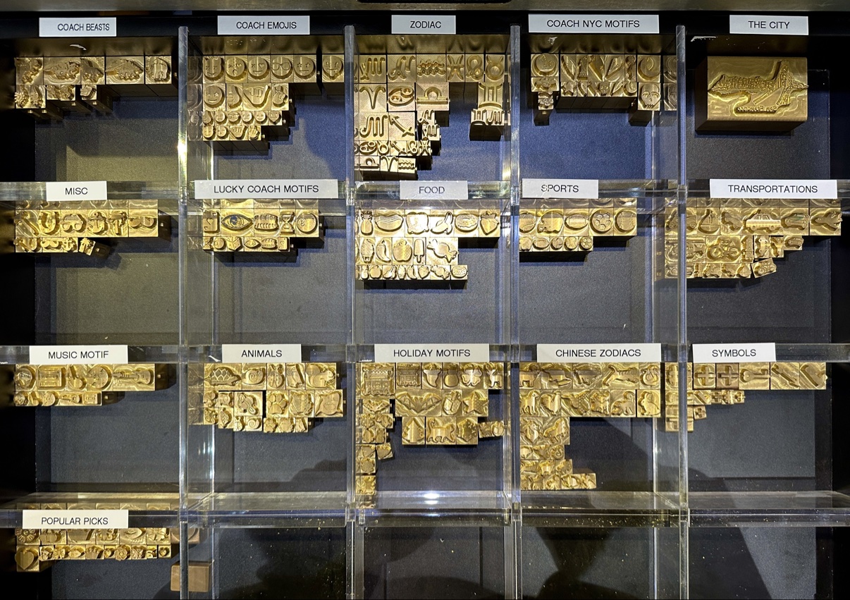 Wall of brass hot-stamp dies organized by category — Coach Beasts, Emojis, Zodiac, NYC Motifs, Food, Animals and more