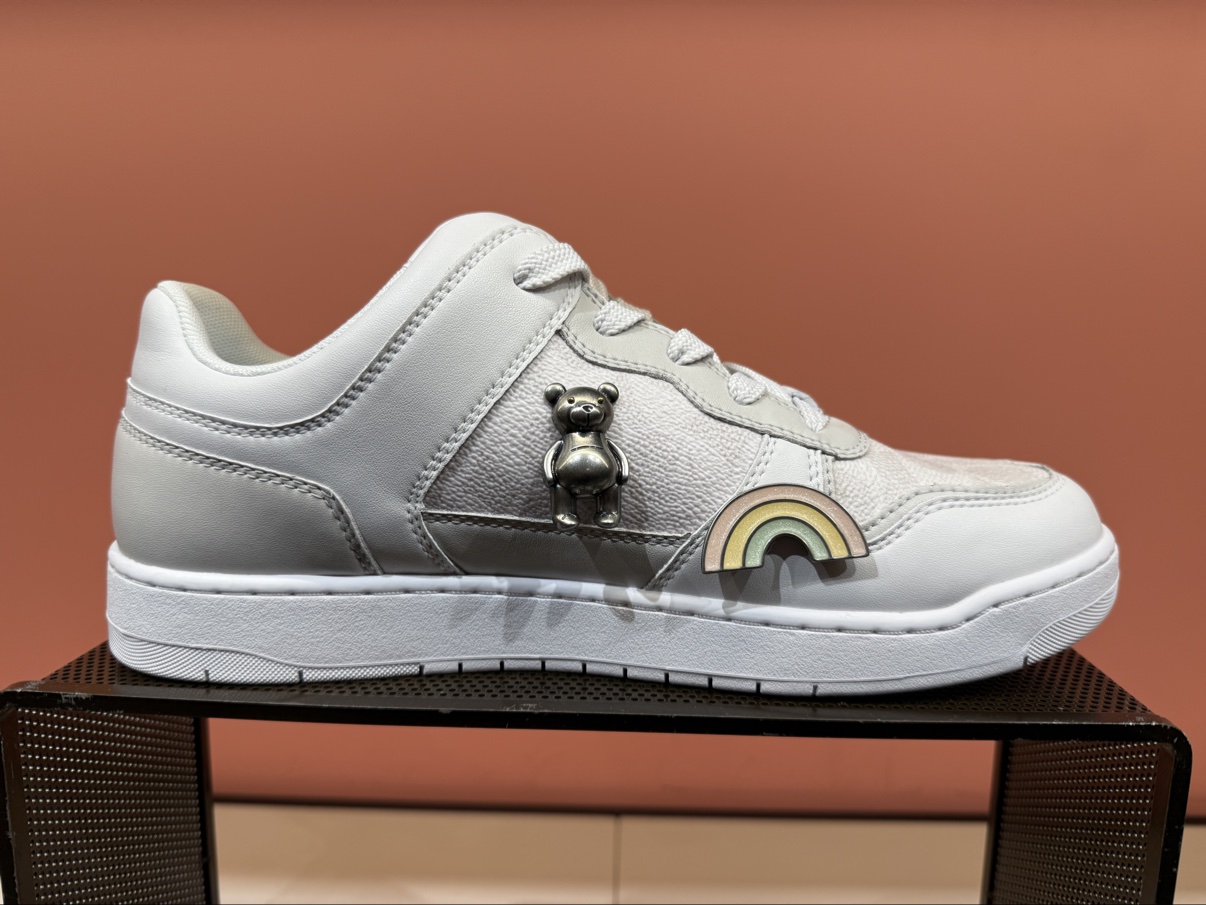 Customized grey and white sneaker with a bear charm and a rainbow detail, on display