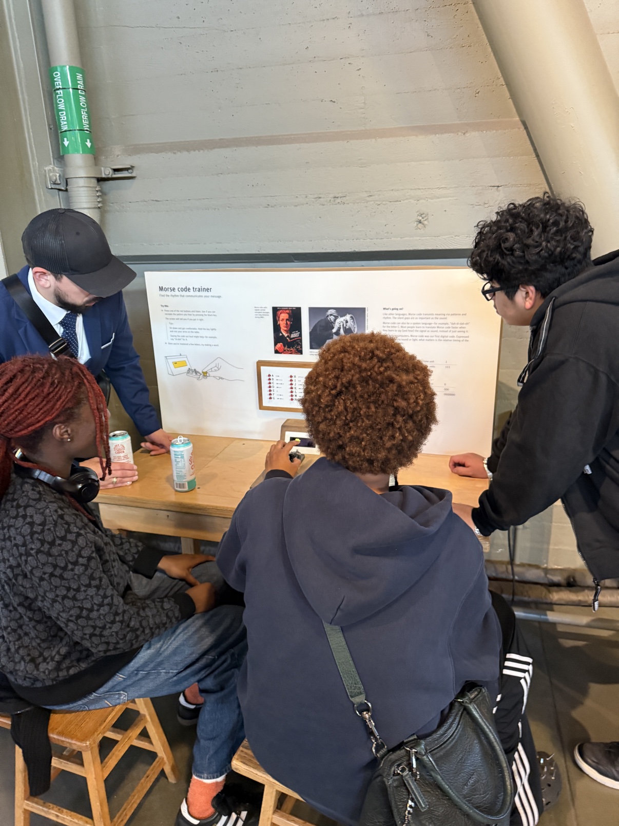 Team members gathered around a Morse code trainer exhibit, trying it out