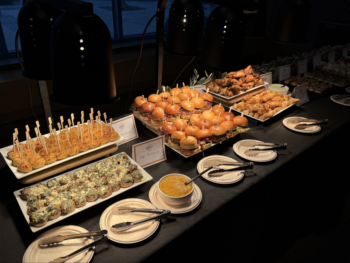 The gala buffet under heat lamps — sliders, mini crab cakes, and stuffed mushroom caps with serving tongs