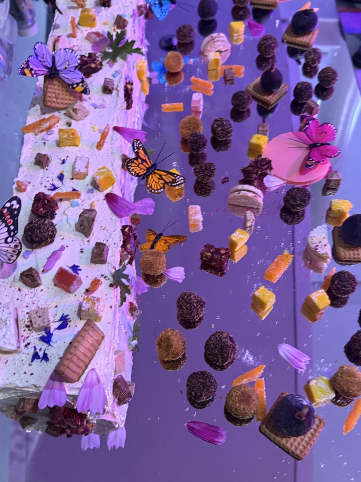 The butterfly dessert table at the gala — a long white frosted dessert and petits fours arranged on a mirror, decorated with butterfly ornaments