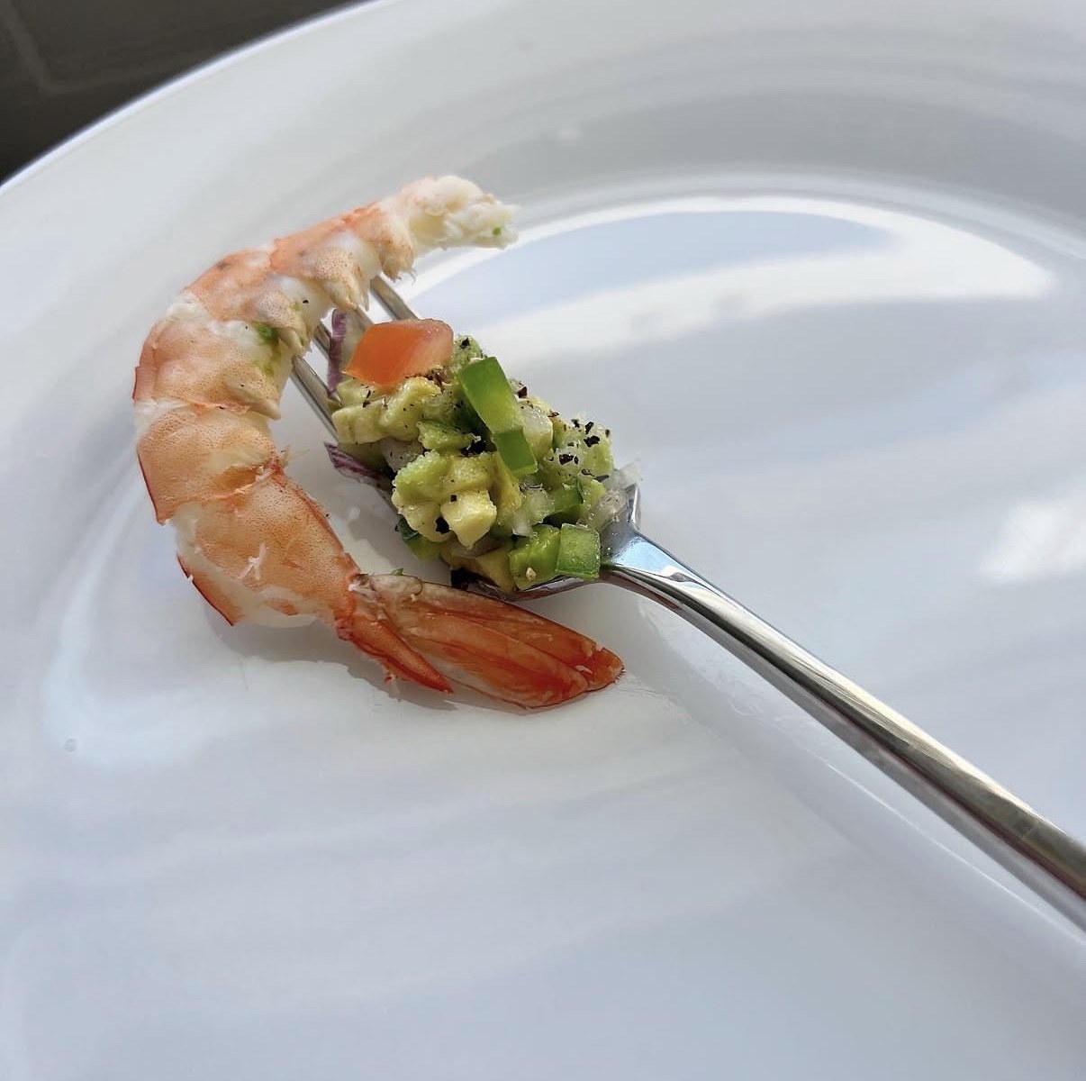 A poached shrimp on a fork with avocado salsa, on a white plate