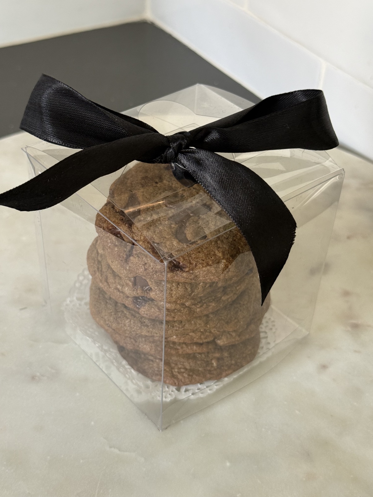 Chocolate chip cookies stacked in a clear gift box tied with a black ribbon
