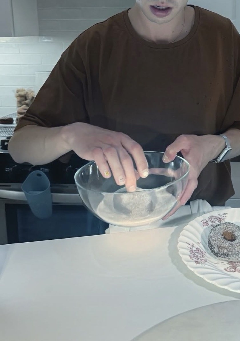 Eldor in his kitchen, tossing a fresh donut in a glass bowl of cinnamon sugar